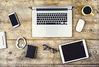 Arbeitstisch mit Laptop, Maus, Handy, Tablet, Kaffee, Brille und Zeitung